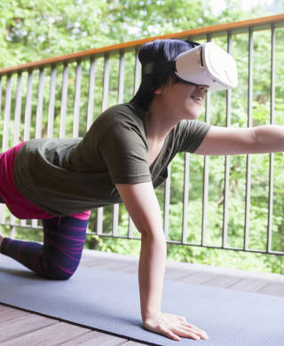 A young woman is doing yoga on balcony and wearing a virtual reality device for instructors.